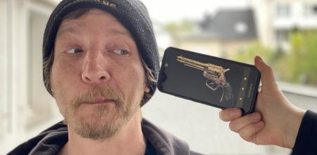 Eine Person, die verzweifelt auf ein Smartphone schaut, auf dem eine Revolver abgebildet ist.