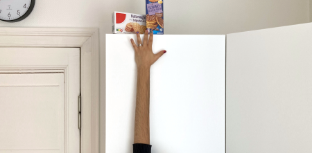 Foto eines Arms, der mit Hilfe eines Grafikprogramms künstlich verlängert wurde, um an Kekse zu kommen, die auf einem hohen Schrank stehen.